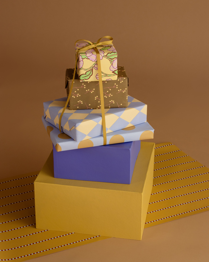 Stapels geschenken in verschillende kleuren en patronen, geplaatst op een gele ondergrond met strepen.