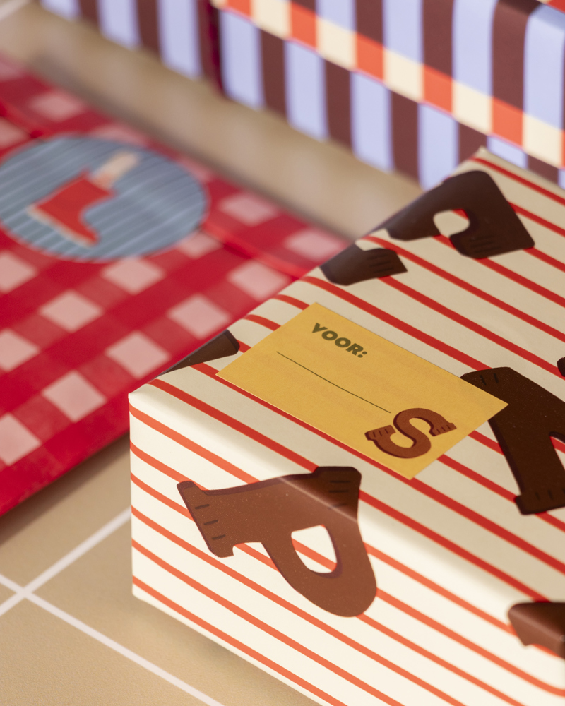 Verpakte sinterklaas geschenken in verschillende kleuren en patronen, met een geel etiket met de tekst "VOOR:" en een bruine letter "S".