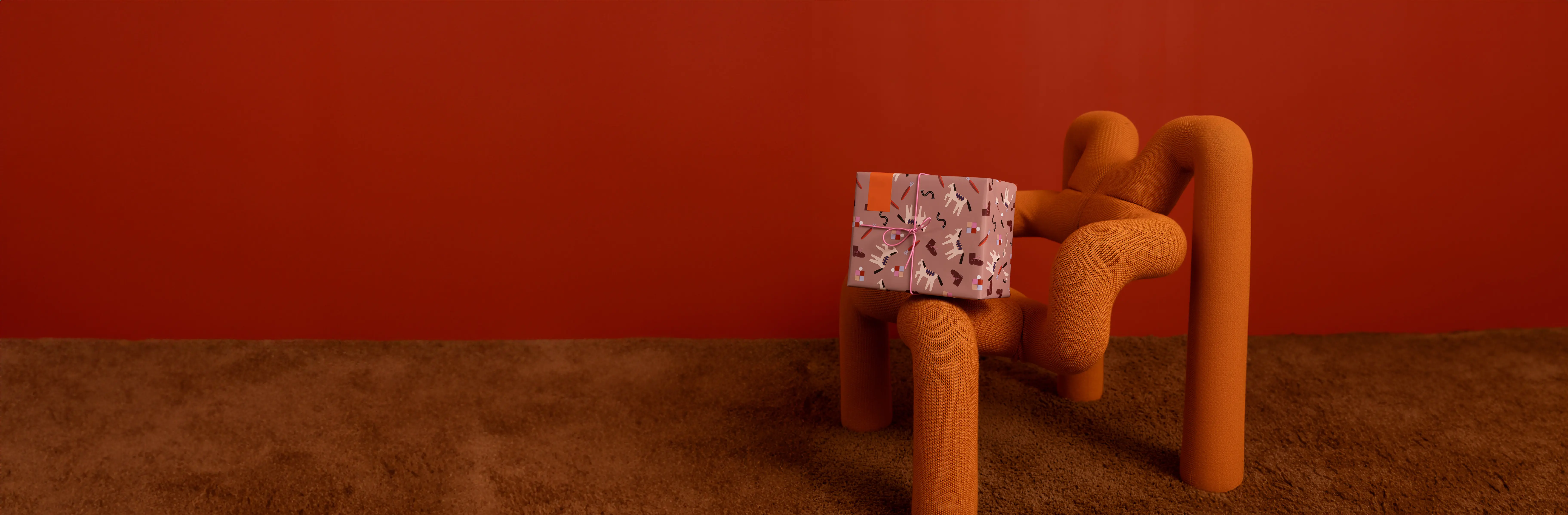Een oranje fauteuil met een patroon van bloemen op een cadeau op de armleuning, tegen een rode muur en een bruine vloer.