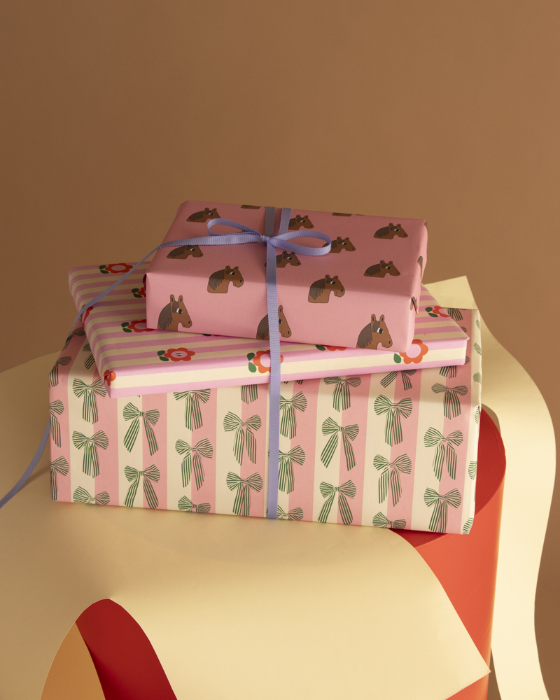 Drie ingepakte cadeaus in verschillende papieren, opgesteld op een kleurrijke ondergrond met een beige muur op de achtergrond.