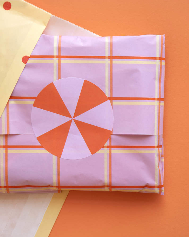 Een verpakt cadeau in roze papier met een ruitpatroon en een ronde, oranje en roze markering op een oranje achtergrond.