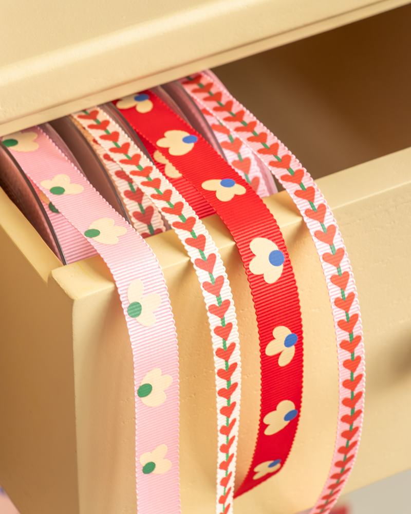 Drie kleurrijke linten liggen in een lade; roze met bloemen, rood met bloemen en een schuin patroon van takken.