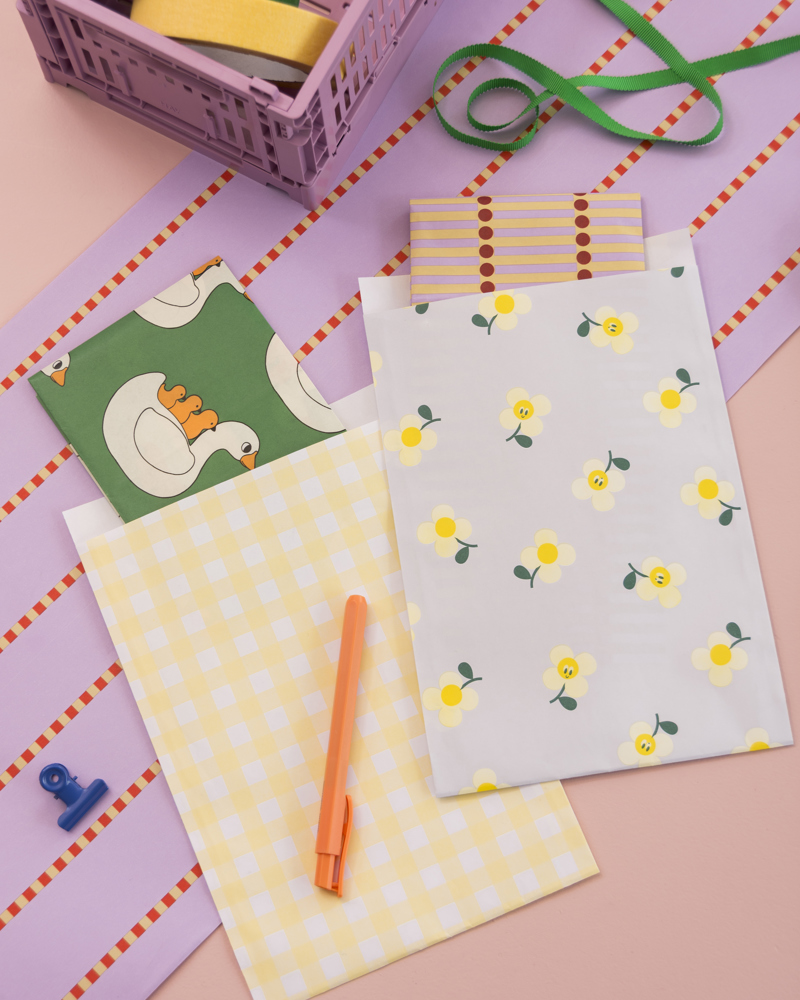 Kleurige enveloppen met bloemen en een zwaan, een oranje pen, en een paar knutselmaterialen op een roze achtergrond.